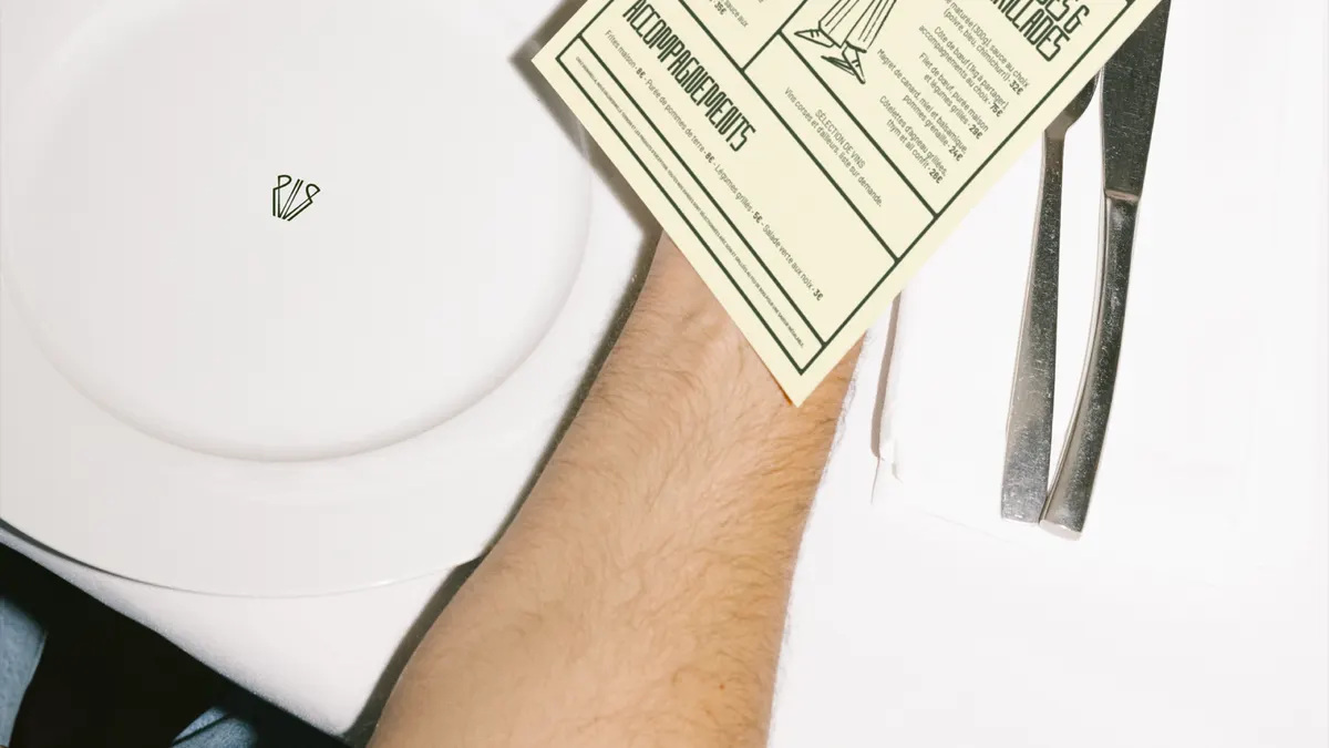 Assiette blanche marquée du monogramme VR de Vignarella, à côté d'un menu crème