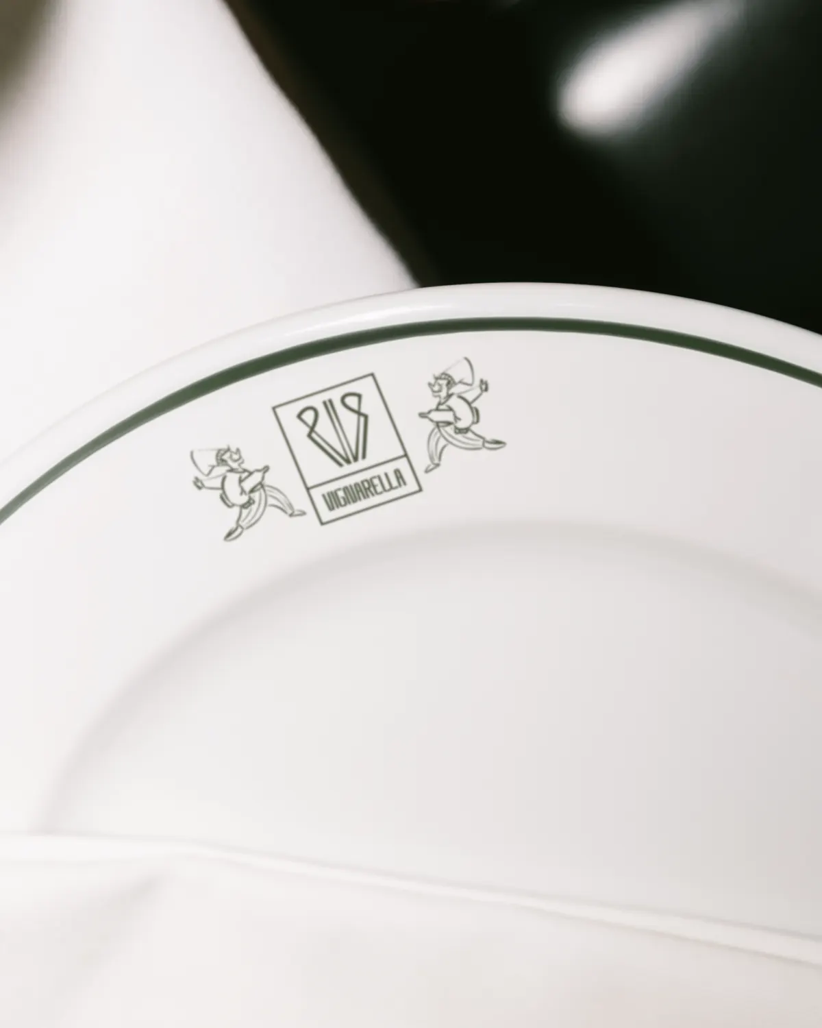 Détail d'une assiette au liseré vert portant le cartouche Vignarella entouré de deux personnages illustrés
