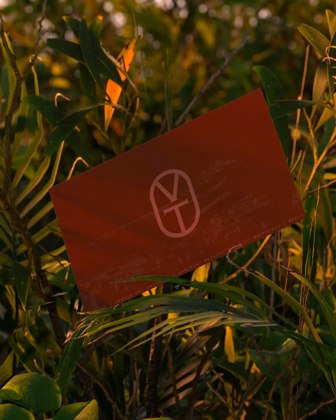 Carte terre cuite marquée du monogramme VT de Villa·T, posée dans la végétation
