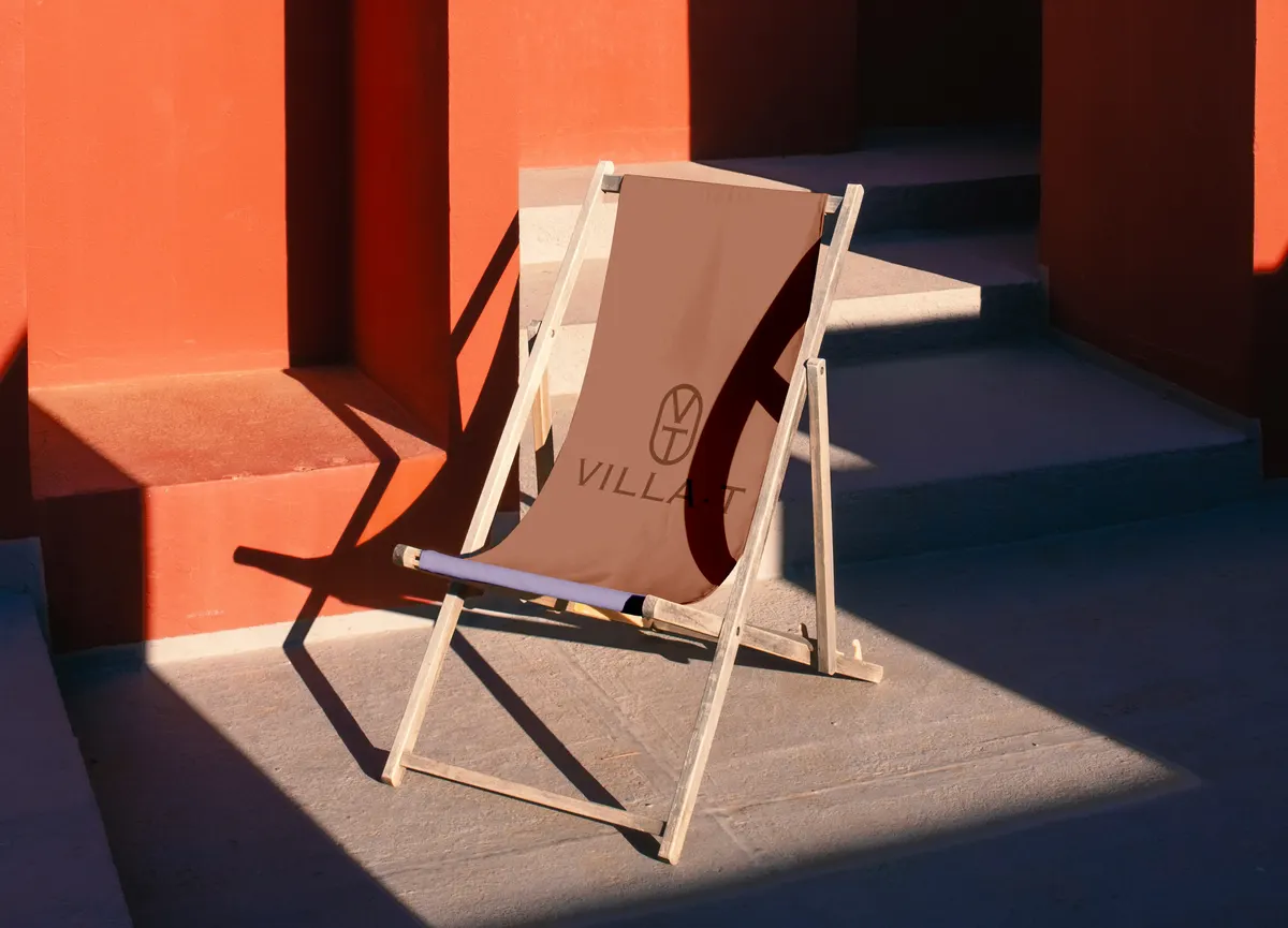 Transat en toile beige marqué du monogramme Villa·T contre un mur ocre au soleil